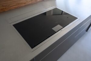 A modern, built-in electric cooktop with a black glass surface is installed in a sleek gray kitchen countertop.
