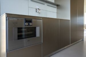 A modern kitchen with metallic cabinets, a built-in oven, and a faucet mounted on a glossy backsplash.